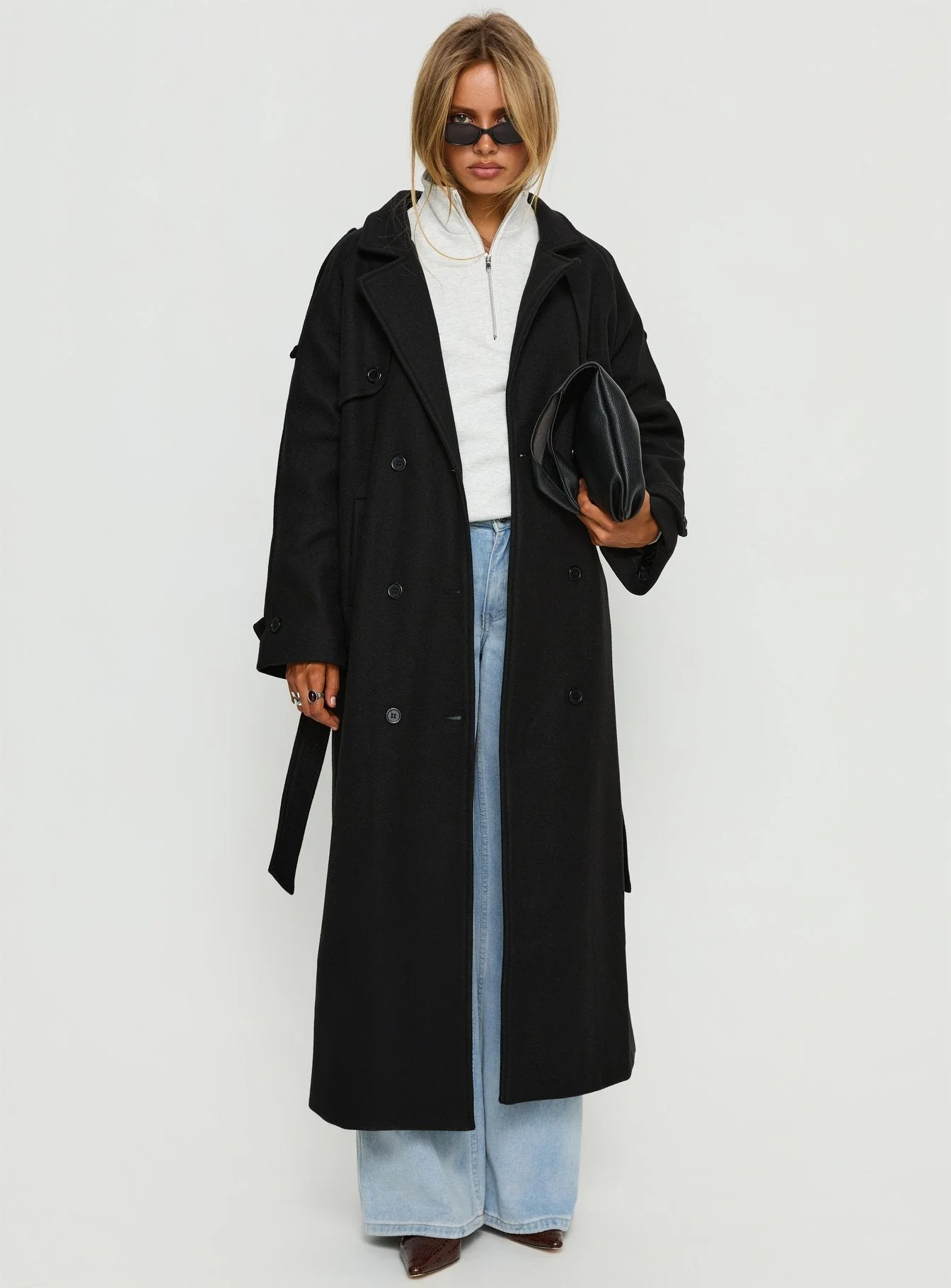 Woman in black trench coat with oversized sweatshirt and jeans
